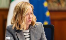Giorgia meloni seduta con dietro la bandiera dell'Europa e quella dell'Italia